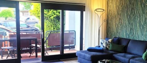 Una sala de estar moderna con un sofá azul, una mesa de centro de vidrio y vistas a un patio exterior a través de puertas correderas de vidrio.