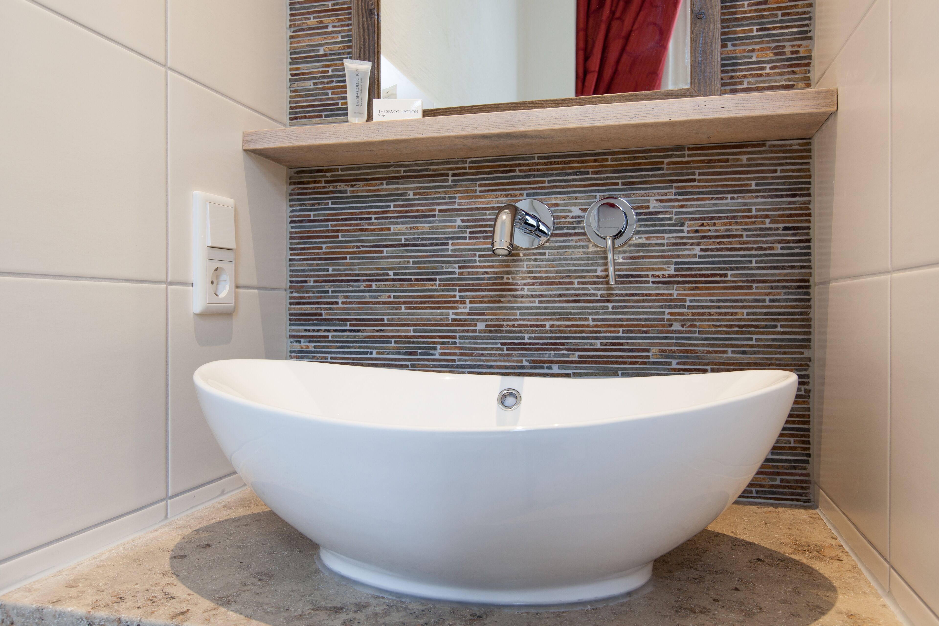 A freestanding bathtub in a bathroom with a tiled backsplash and a wooden shelf above it.