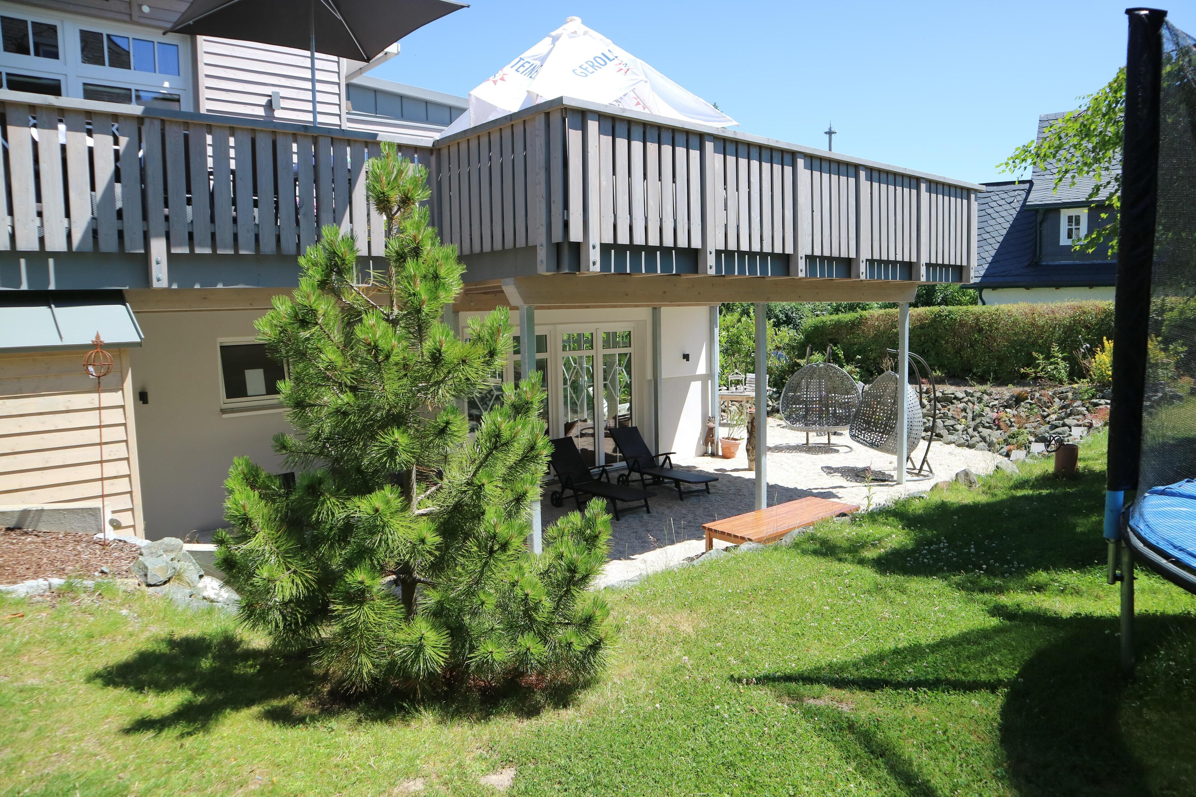 Una casa moderna con un porche cubierto, un pequeño jardín y un trampolín.