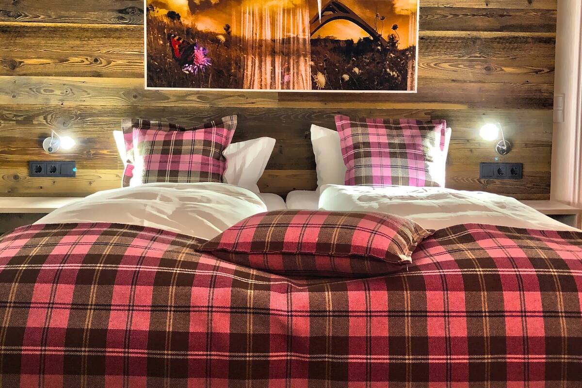 A bed with plaid bedding and a painting of a landscape on the wall.