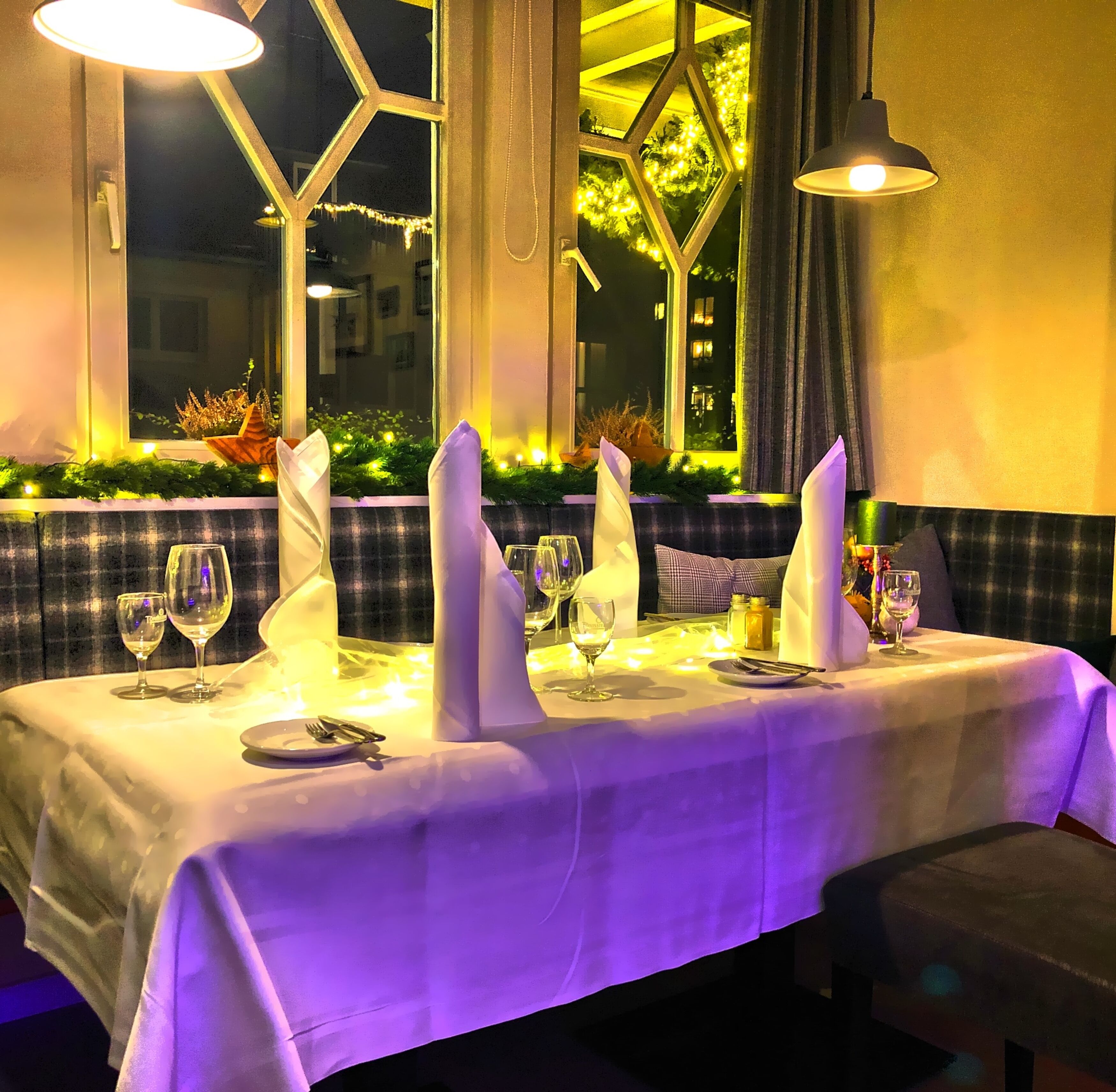 Mesa lista para comer con mantel blanco, varias copas de vino y servilletas.