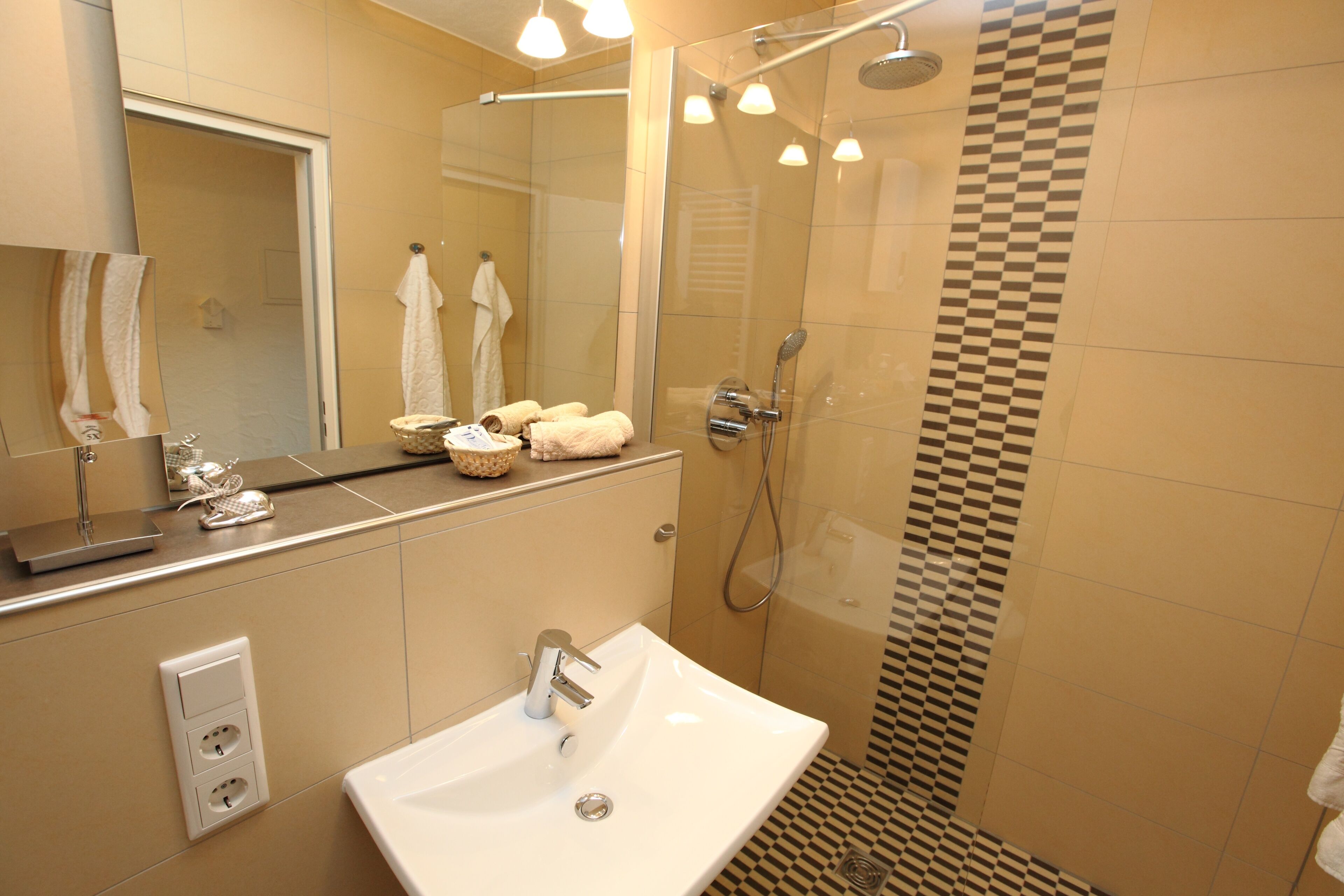 A modern bathroom with a large mirror, a sink, a shower with a glass door, and a checkered tile pattern on the wall.