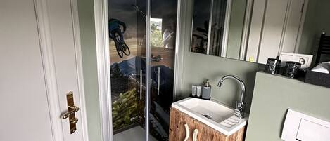 Ein Badezimmer mit einem Holzkonsolenunterschrank, einem weißen Waschbecken, einem Spiegel und einer Duschkabine aus Glas.