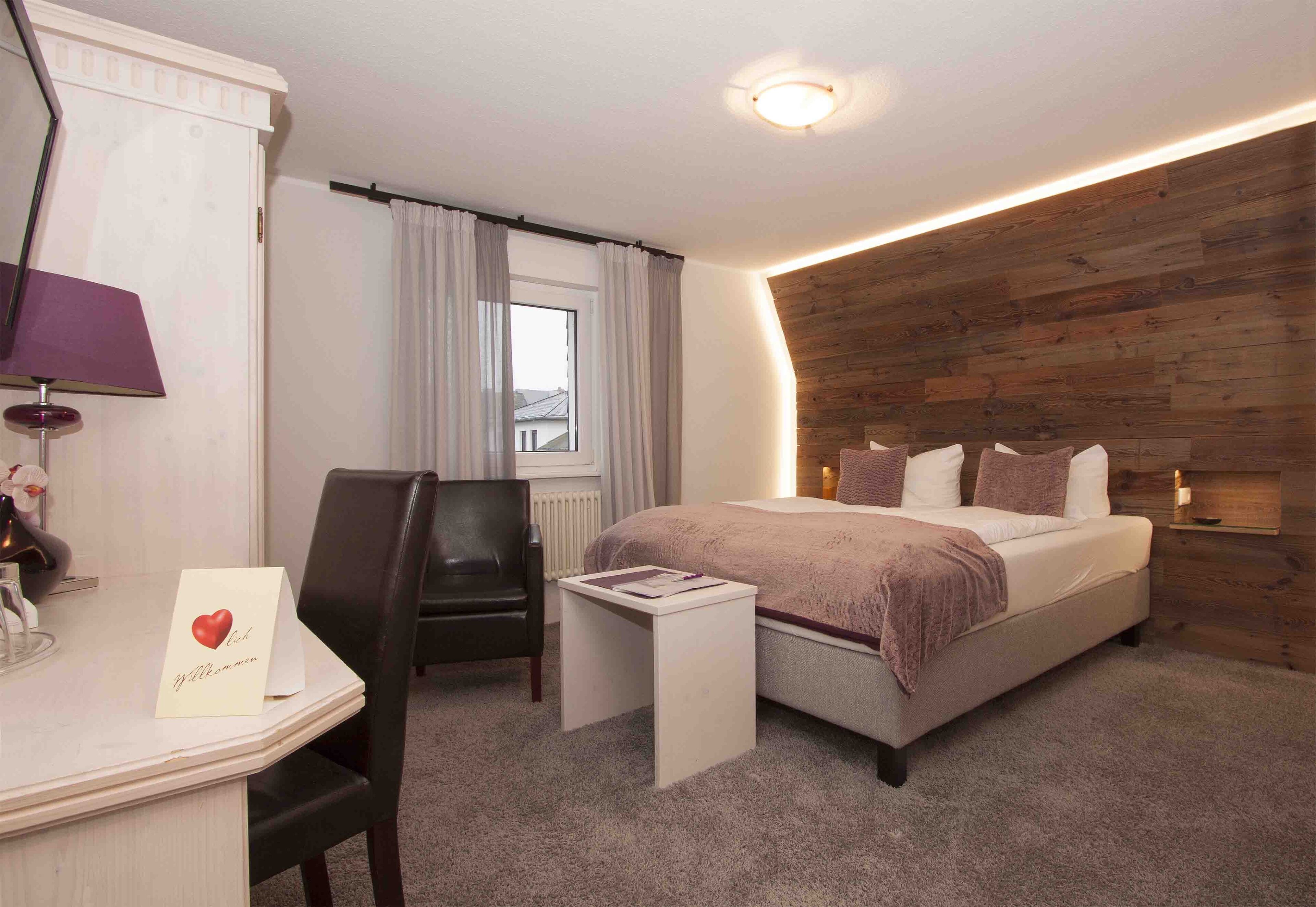 Ein modernes Schlafzimmer mit einer Wand als Holzdekor, einem Bett mit Kissen, einem Schreibtisch mit Lampe und einem Sessel.