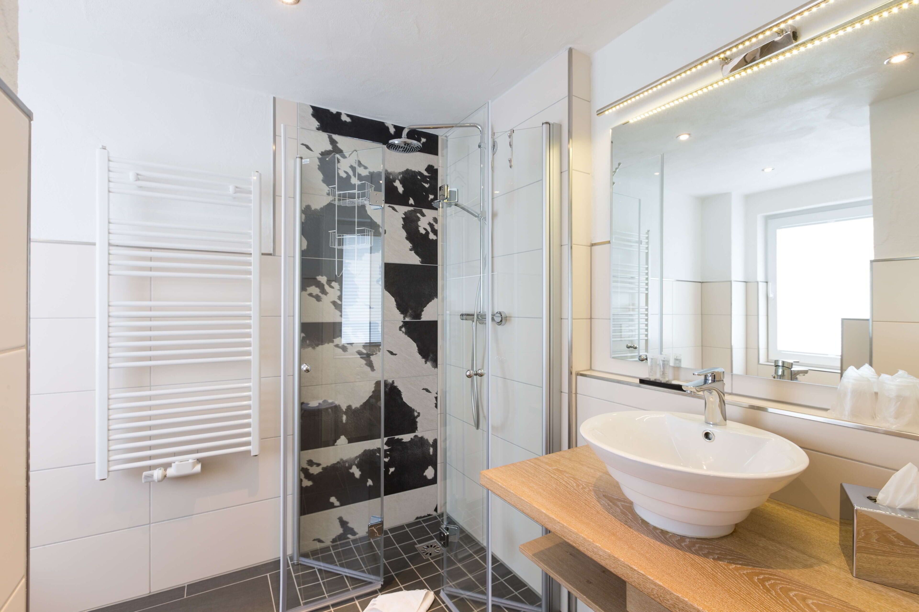 Een moderne badkamer met een douchecabine van glas, een witte wastafel en een houten wastafelmeubel.