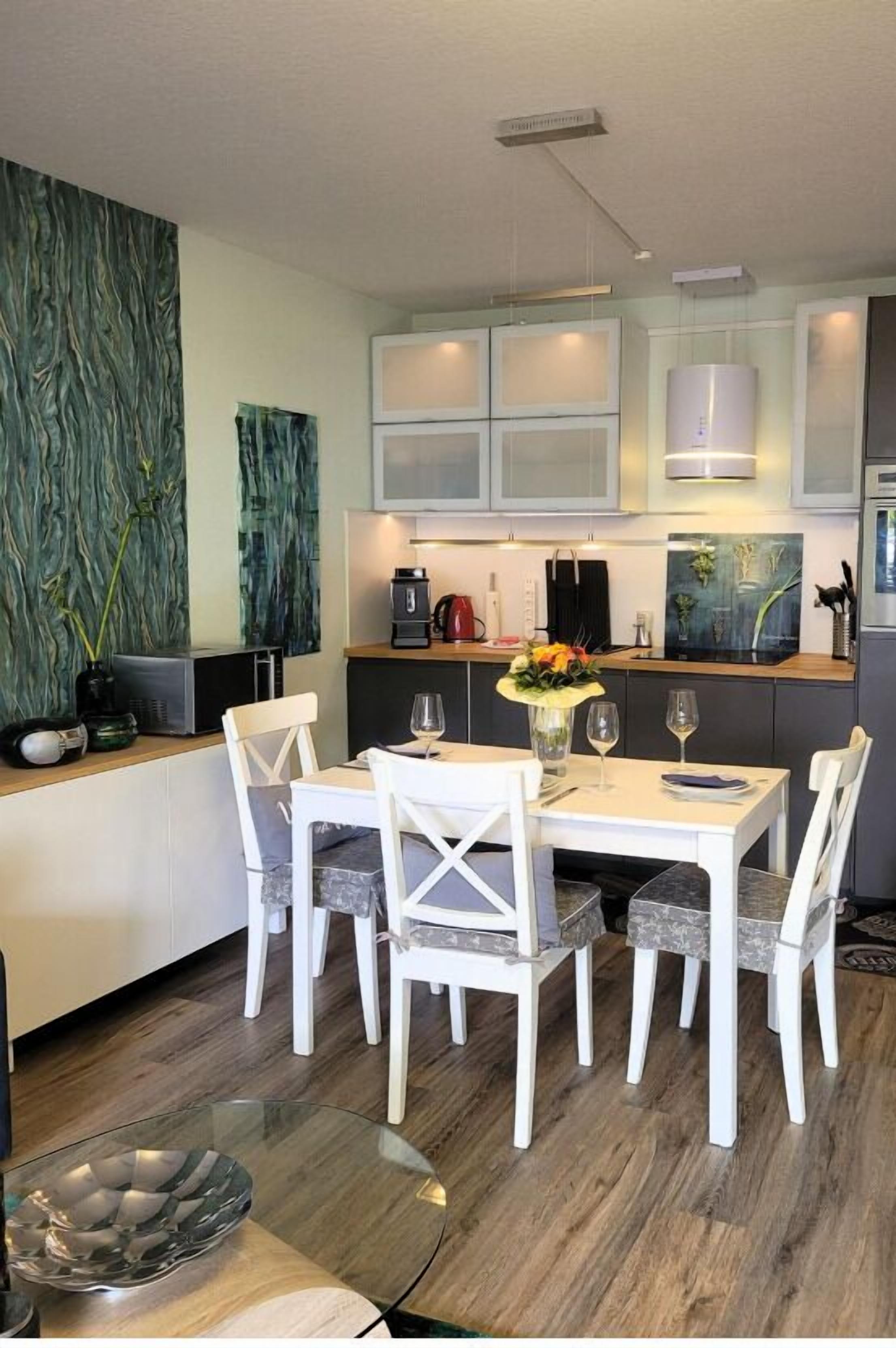 A modern kitchen with white cabinets, a dining table with four chairs, and a glass coffee table.