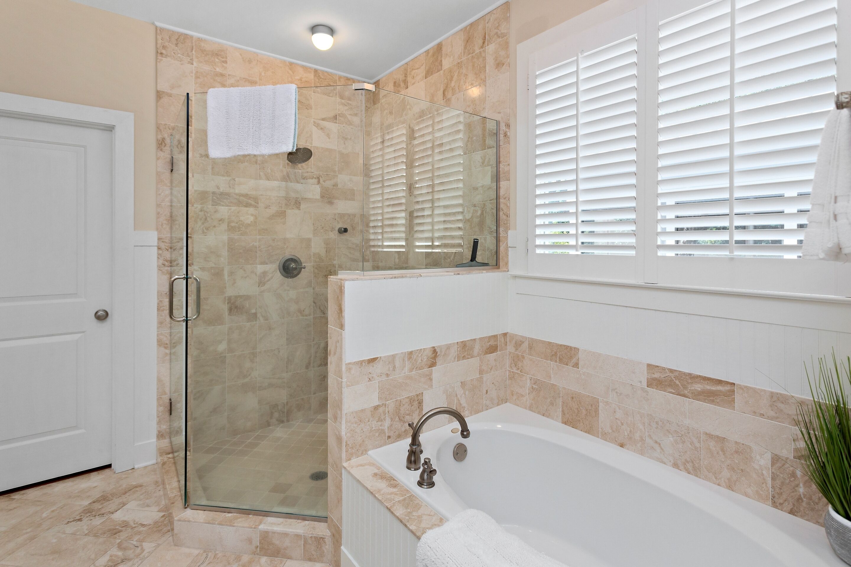 A bathroom with a glass-enclosed shower, a bathtub, and a window with blinds.