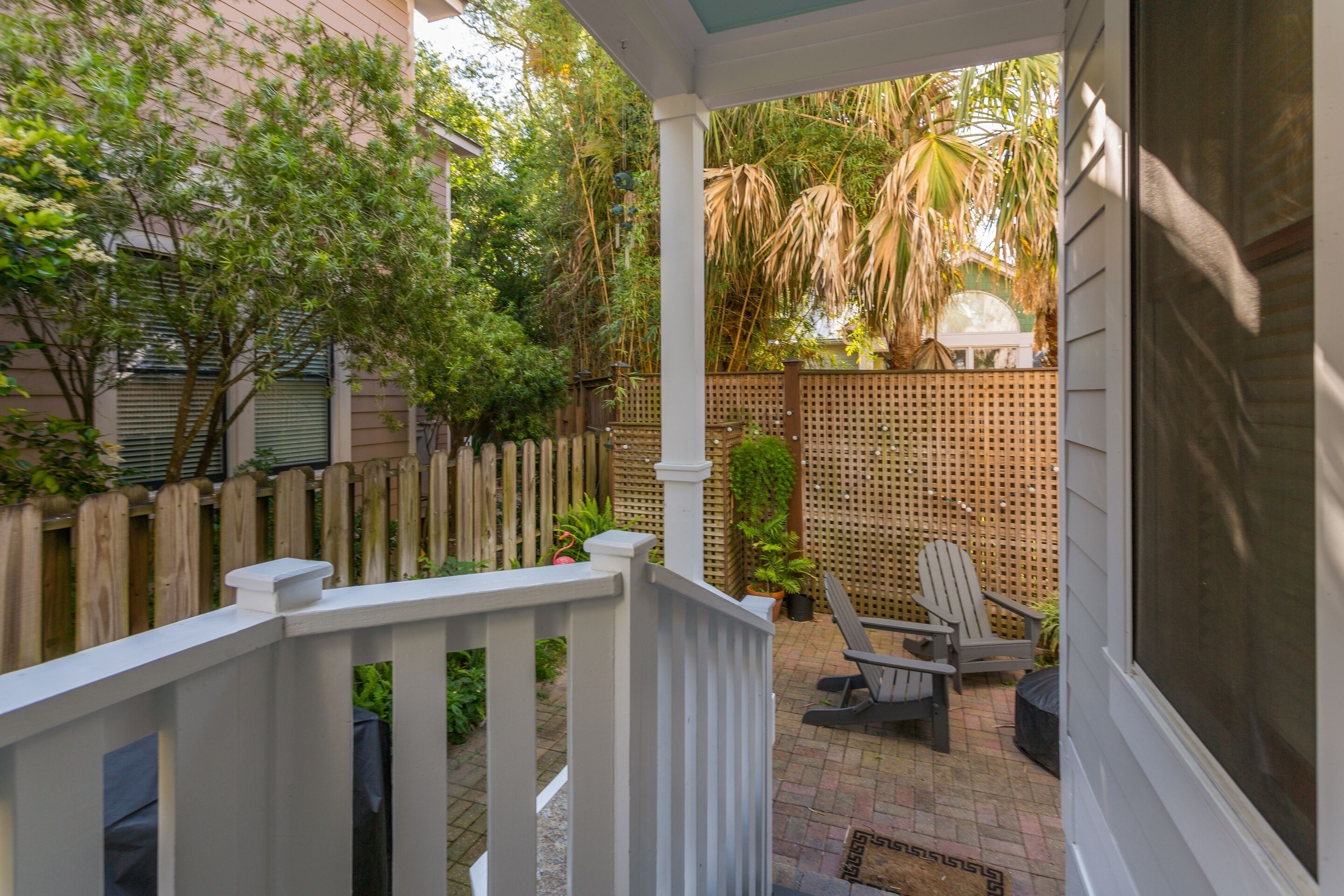 A covered patio with a wooden fence, outdoor seating, and a view of a lush garden.