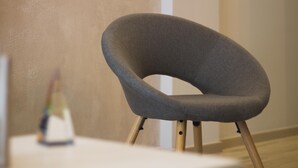 Une chaise moderne dotée d’un dossier incurvé et de pieds en bois, placée dans une pièce dont le mur est uni et le sol est blanc.