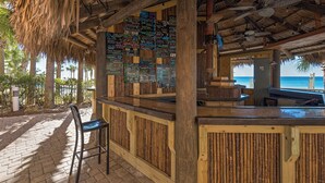 Un bar junto a la playa con fachada de madera, paneles de bambú y techo de paja.