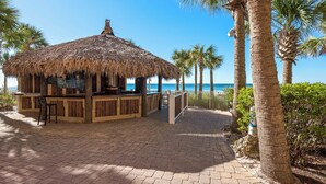 Un bar en la playa con techo de paja, asientos de madera y vista al océano.