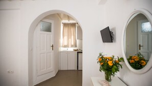 Un couloir avec une porte blanche, un coin cuisine avec une fenêtre et un miroir rond accroché au mur.
