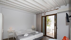 Une chambre avec deux lits, une petite table, une télévision et une porte-fenêtre coulissante donnant sur un espace extérieur.