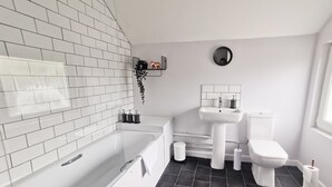 Et moderne badeværelse med hvide fliser, et badekar, et toilet og en vask.