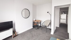 En moderne stue med et fladskærms-tv, et rundt spejl, et spisebord med stole, en gulvlampe og et hyggeligt siddeområde.