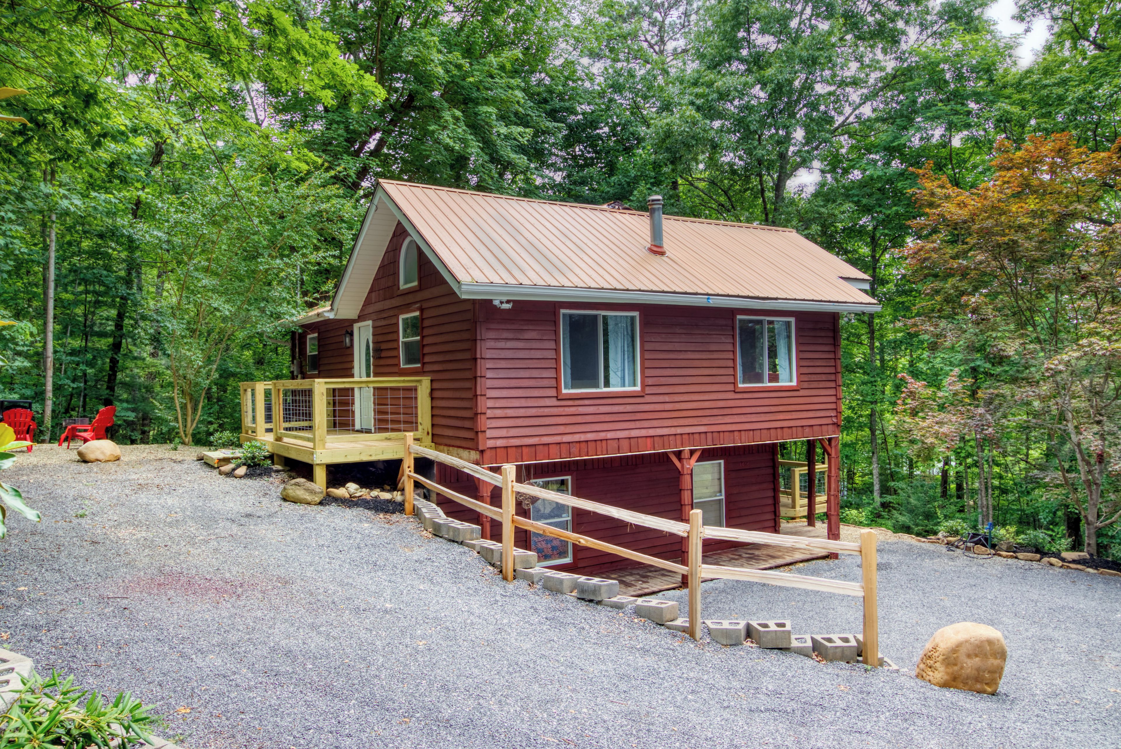 A red cabin with a wooden deck and a gravel driveway.