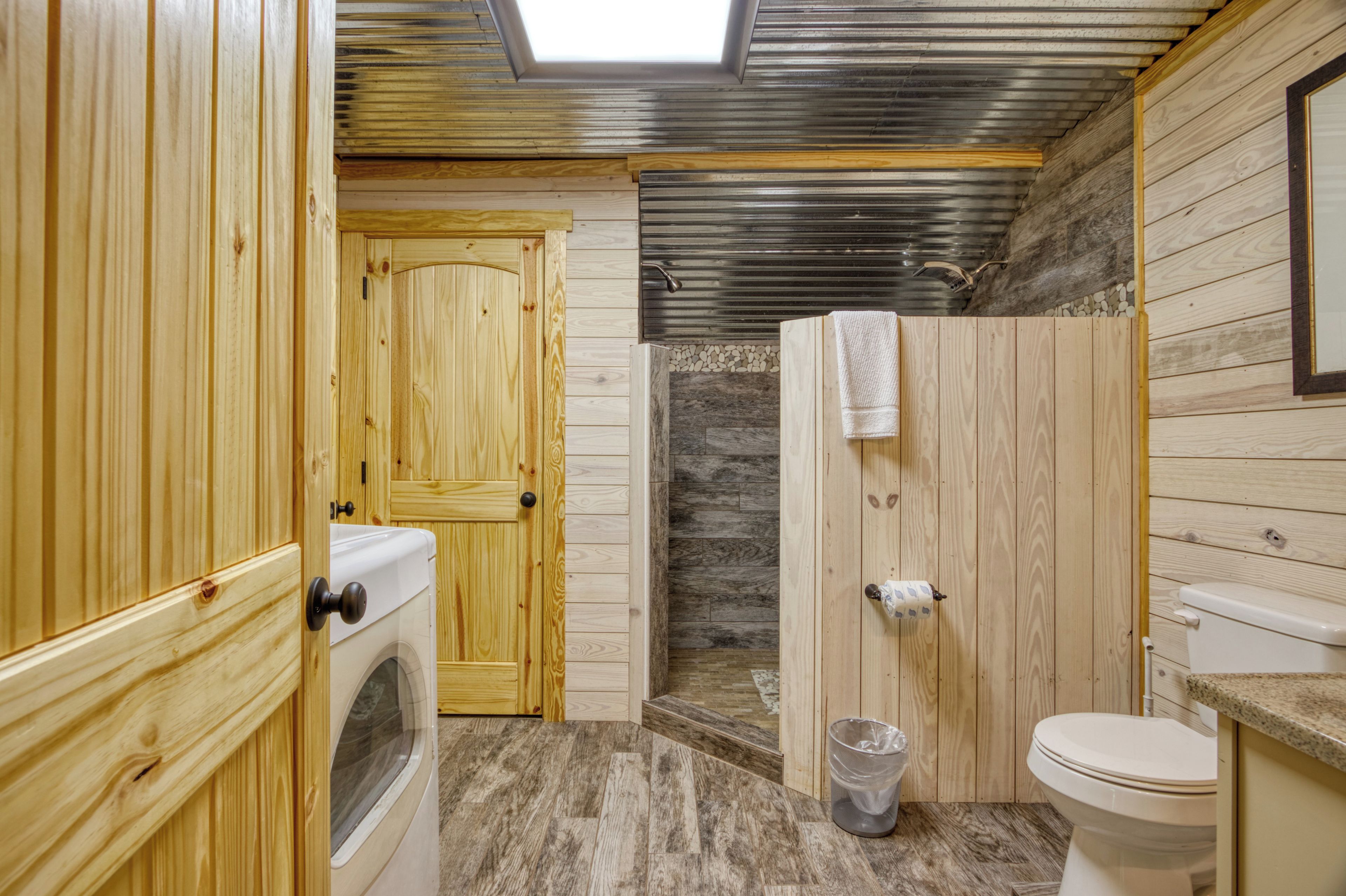 Une salle de bain rustique, aménagée dans une cabane en bois, avec un puits de lumière, un lave-linge, une douche et des toilettes.