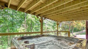 Uma banheira de hidromassagem com deck de madeira e estrutura de vidro, cercada por árvores.