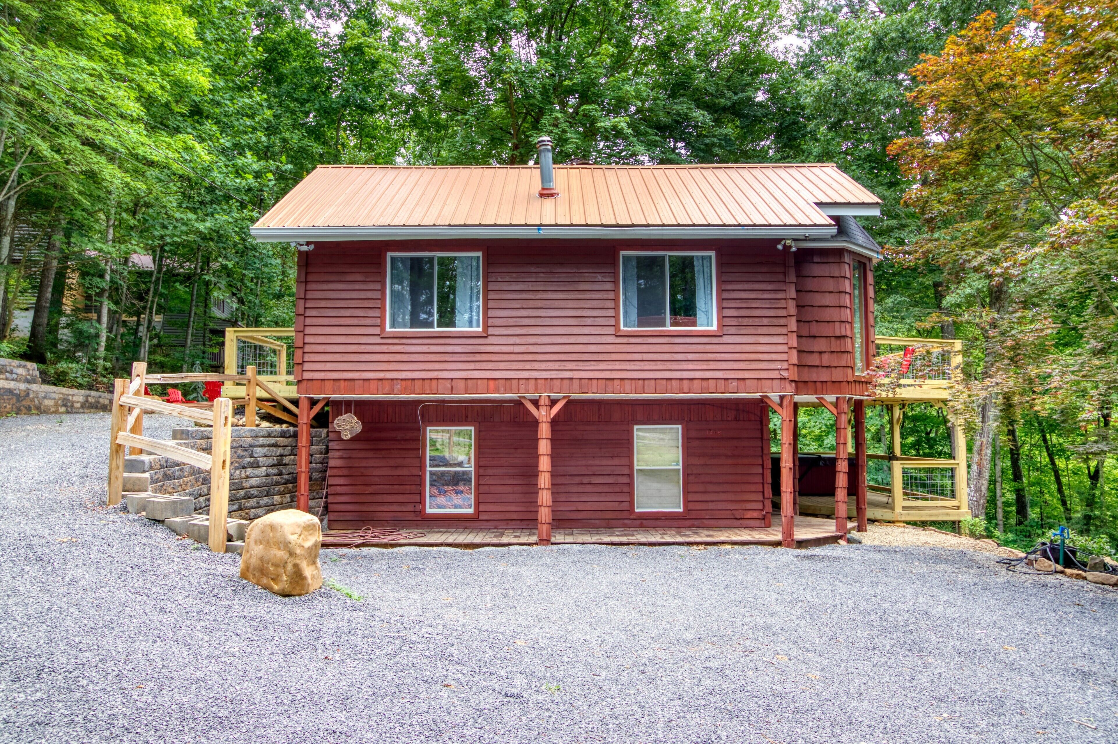 A two-story wooden cabin with a metal roof, a wooden deck, and a stone staircase leading to a wooden door.