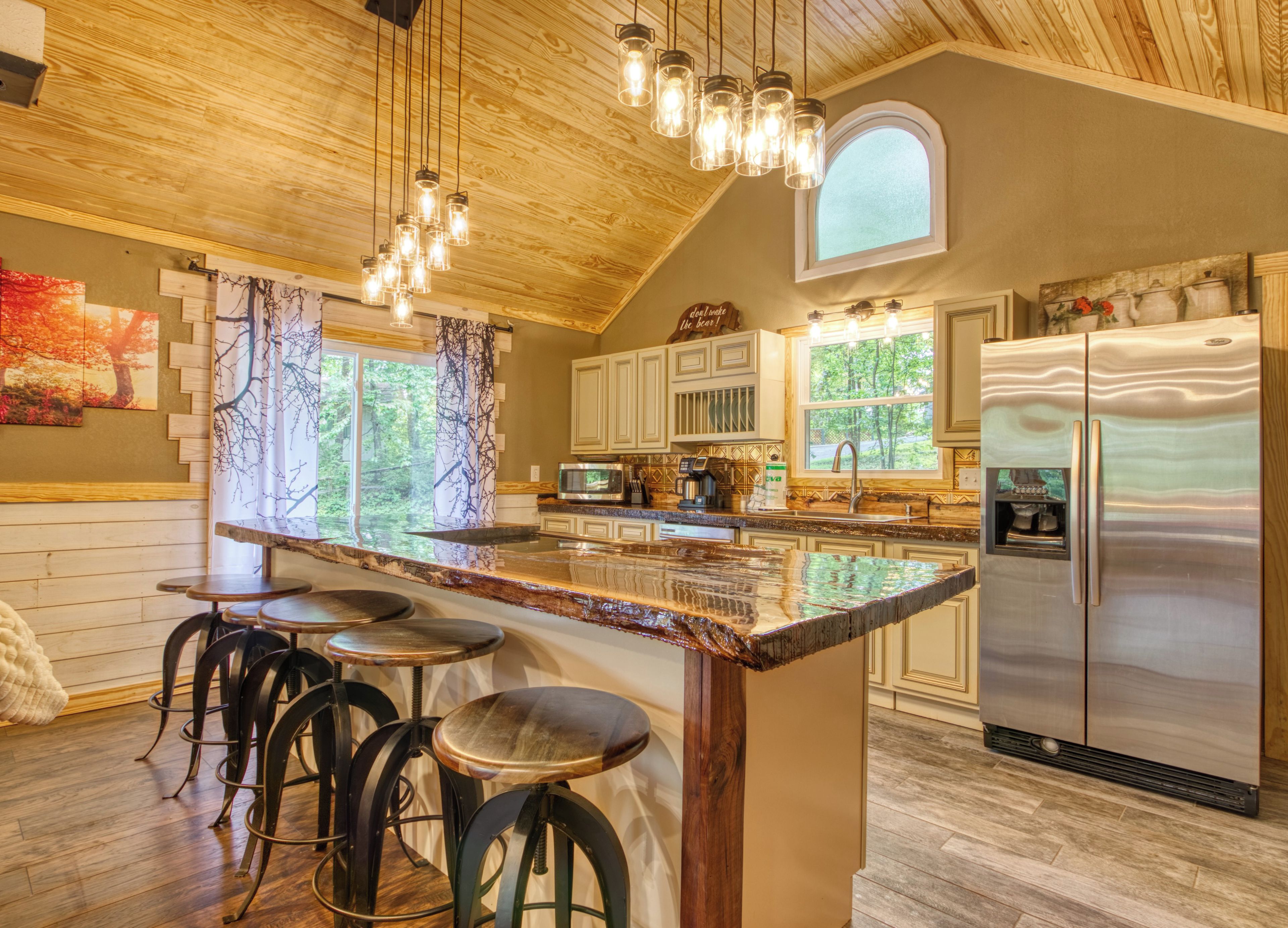 A kitchen with a large island, bar stools, stainless steel appliances, and a wooden ceiling.
