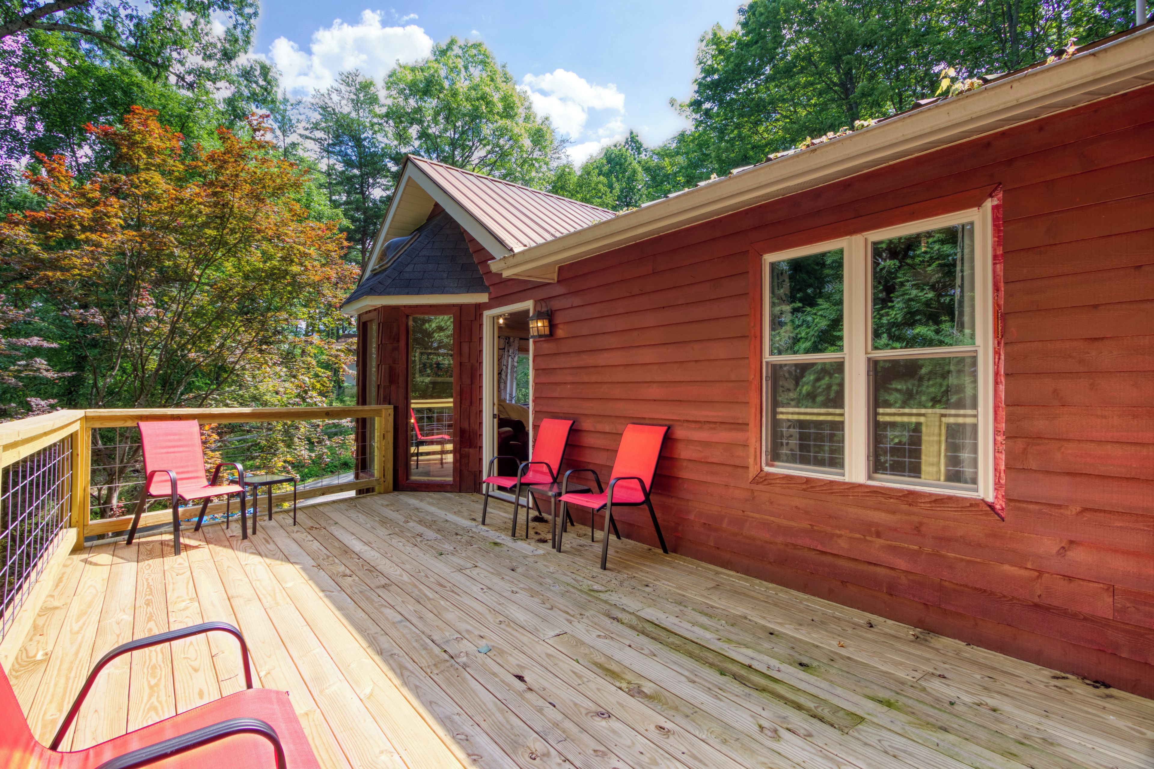 A wooden cabin with a deck, red chairs, and a window.