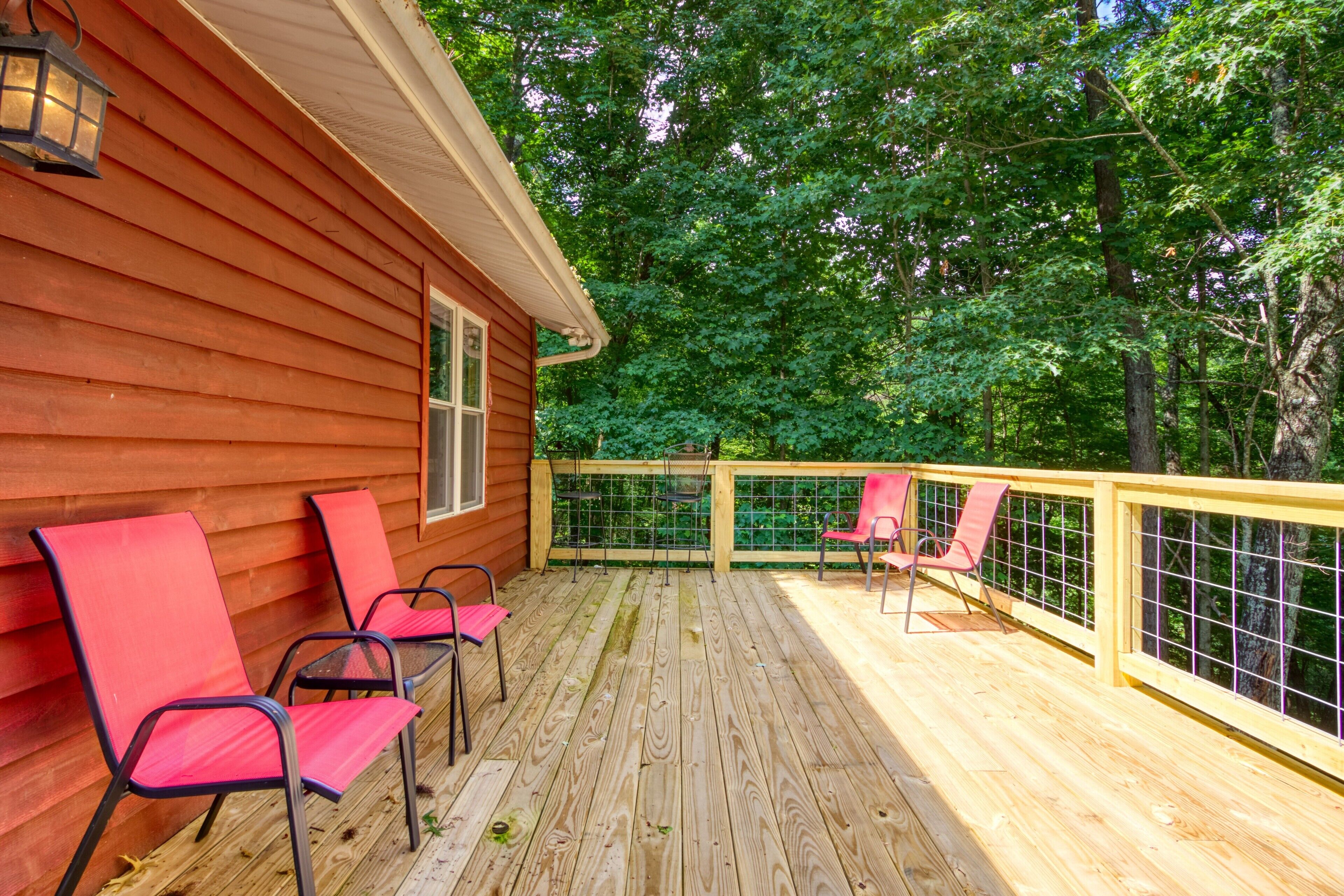 A wooden deck with red chairs and a railing, surrounded by trees.