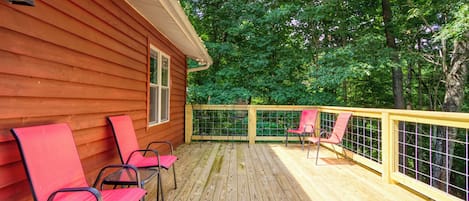A wooden deck with red chairs and a railing, surrounded by trees.
