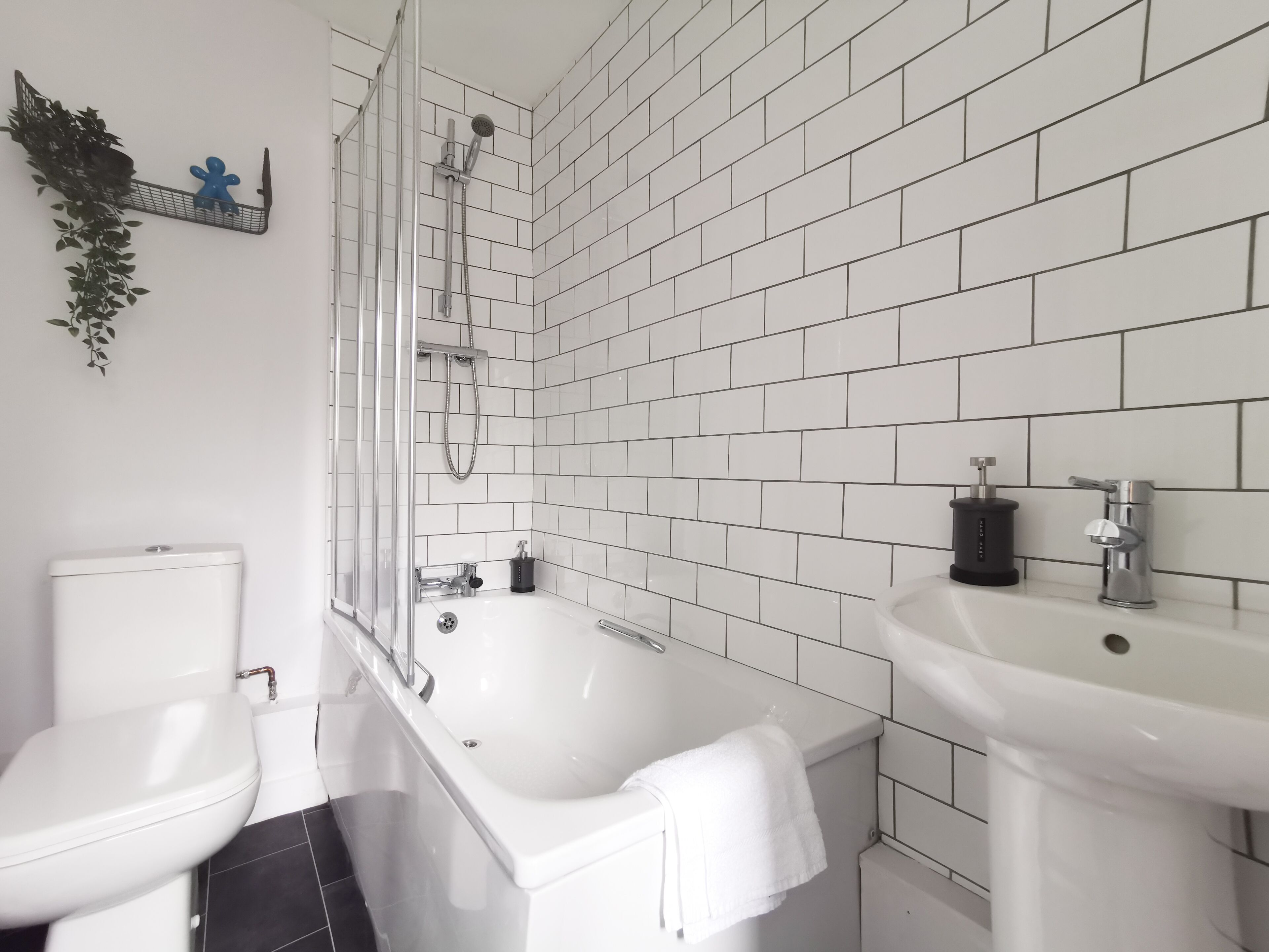 A modern bathroom with white tiles, a bathtub, a toilet, and a sink.