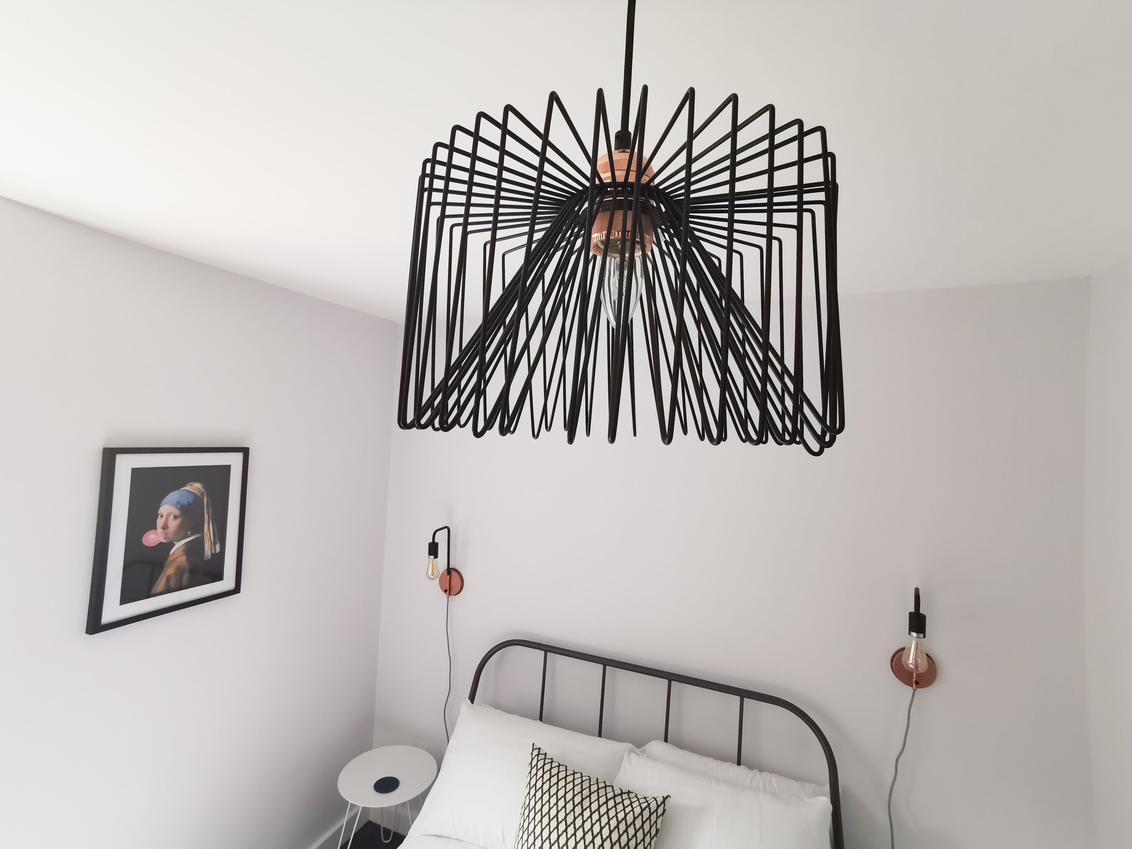 A bedroom with a bed, a round side table, a wall-mounted light fixture, and a framed picture.