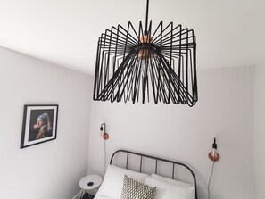 Ein Schlafzimmer mit einem Bett, einem runden Beistelltisch, einer Wandleuchte und einem gerahmten Bild.