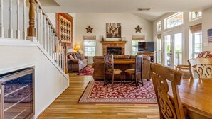 A spacious living room with a fireplace, wooden flooring, and a dining area with chairs and a table. - Bonnie Brae-Lakefront Getaway w/Jet Ski & Boat Lift (Kingsland)