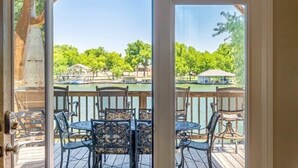 A view from a room with a wooden deck outside, featuring a table and chairs, a clear sky, and a body of water in the background. - Bonnie Brae-Lakefront Getaway w/Jet Ski & Boat Lift (Kingsland)