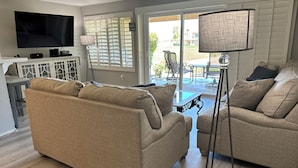 Un salon avec deux canapés beiges, une table basse, un téléviseur et un lampadaire.