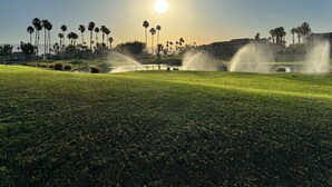 Un terrain de golf avec un ciel dégagé, des palmiers et un bâtiment en arrière-plan.