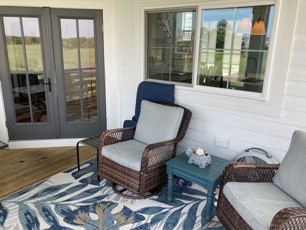 A cozy outdoor seating area with wicker furniture, a patterned rug, and a glass door leading to a patio. - Amazing marsh view and close to beach! (Holden Beach)