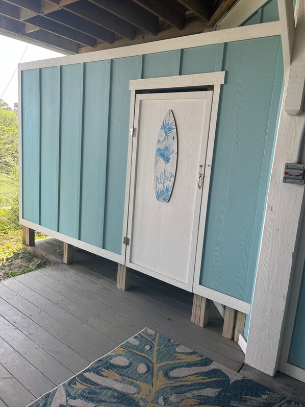 En træterrasse med en dør, der har en surfbræt-dekal og ordet "Aloha".