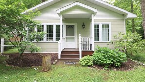 A small, single-story house with a front porch, white siding, and a small garden area.
