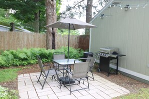 Eine Terrasse im Freien mit Tisch, Stühlen, einem Grill und einer Pergola.