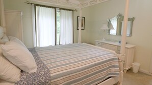 A four-poster bed with a striped bedspread, a bedside table with a lamp, and a mirror above the mirror cabinet.