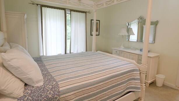 A four-poster bed with a striped bedspread, a bedside table with a lamp, and a mirror above the mirror cabinet. - 4358 W. Lake Road 3 Bedroom Home by RedAwning (Mayville)