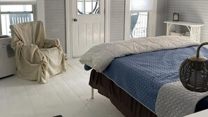 A bedroom with a bed, a chair, a small table, and a door with a window. - Sweet Mary 2 Bedroom Home by RedAwning (Jamestown)