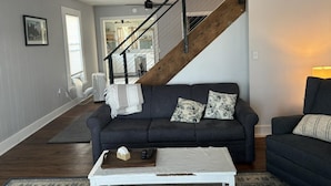 A living room with a dark sofa, a white coffee table, and a staircase with a wooden finish. - Sweet Mary 2 Bedroom Home by RedAwning (Jamestown)