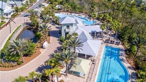 An aerial view of a resort with a large swimming pool, multiple guest villas, and lush landscaping.