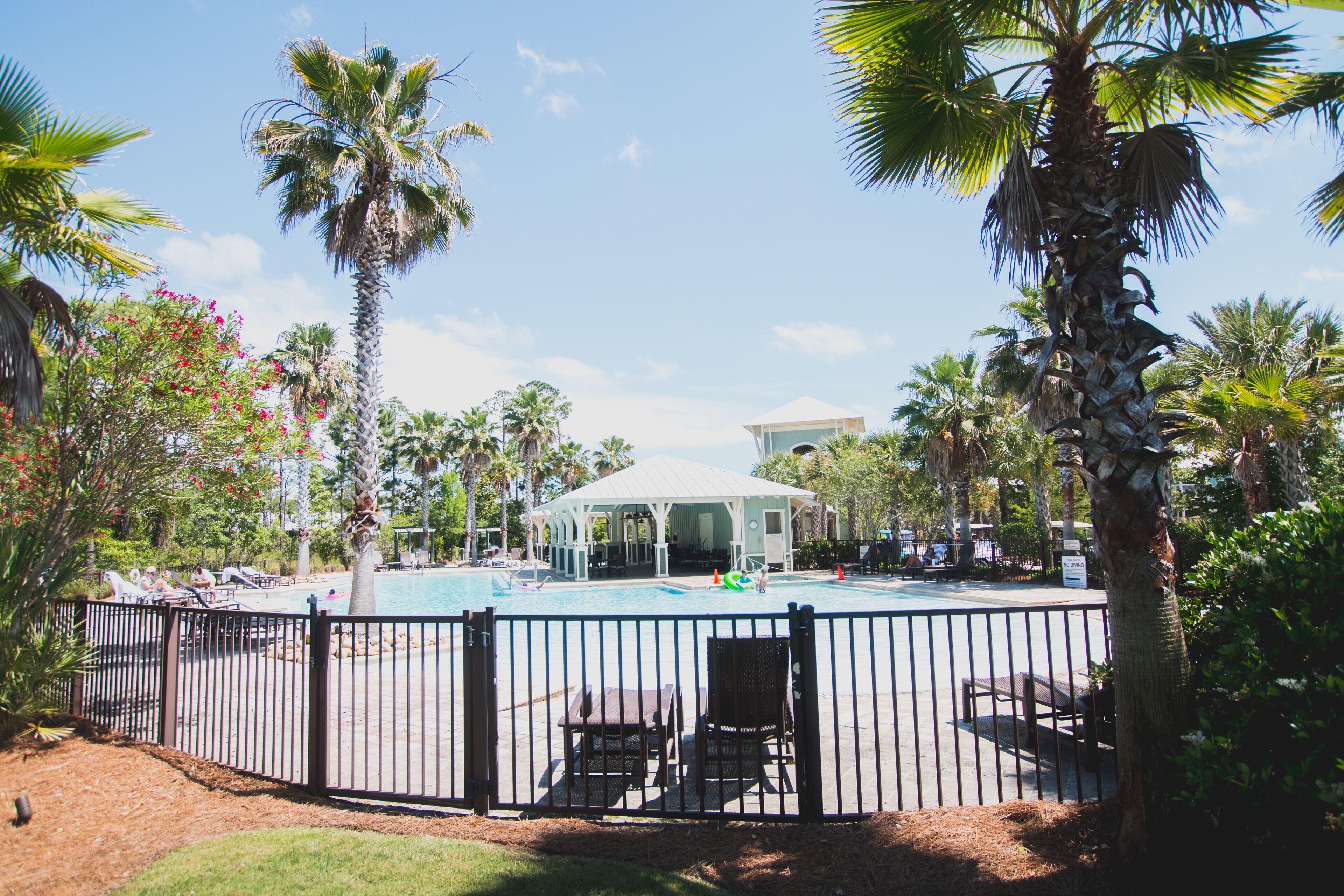 A pool area with palm trees, lounge chairs, and a gazebo.