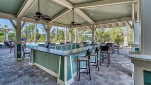 An outdoor bar area with a pool, covered seating, and a ceiling fan.