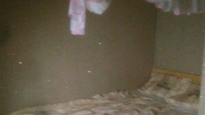 A small, dimly lit room with a single bed, a wooden headboard, and a hanging curtain. - Apex Guest Rooms (Juja)