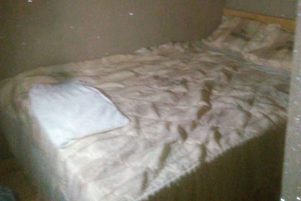 A small, dimly lit room with a single bed, a wooden headboard, and a hanging curtain.