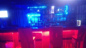 A bar area with red and blue neon lights, a bar counter, and several chairs. - Apex Guest Rooms (Juja)