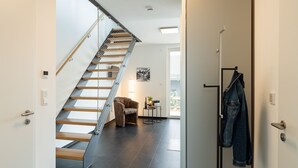Un interior moderno con una escalera de madera, un sillón estampado y una chaqueta vaquera colgada en una puerta.