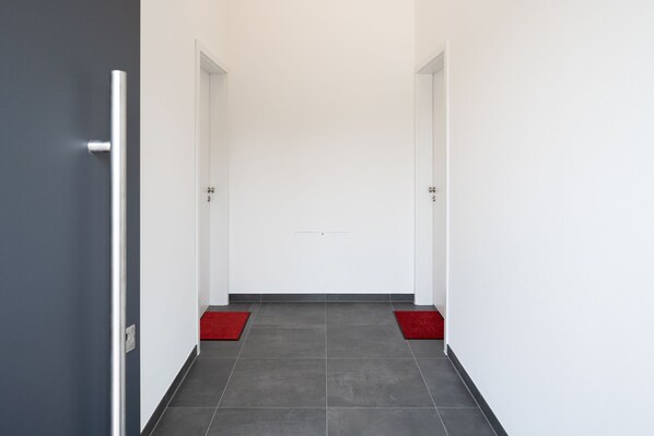 A hallway with a door at the end, a red mat at the entrance, and a grey tiled floor.